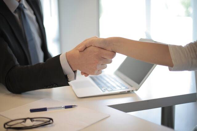 Two people shaking hands across a light wood desk